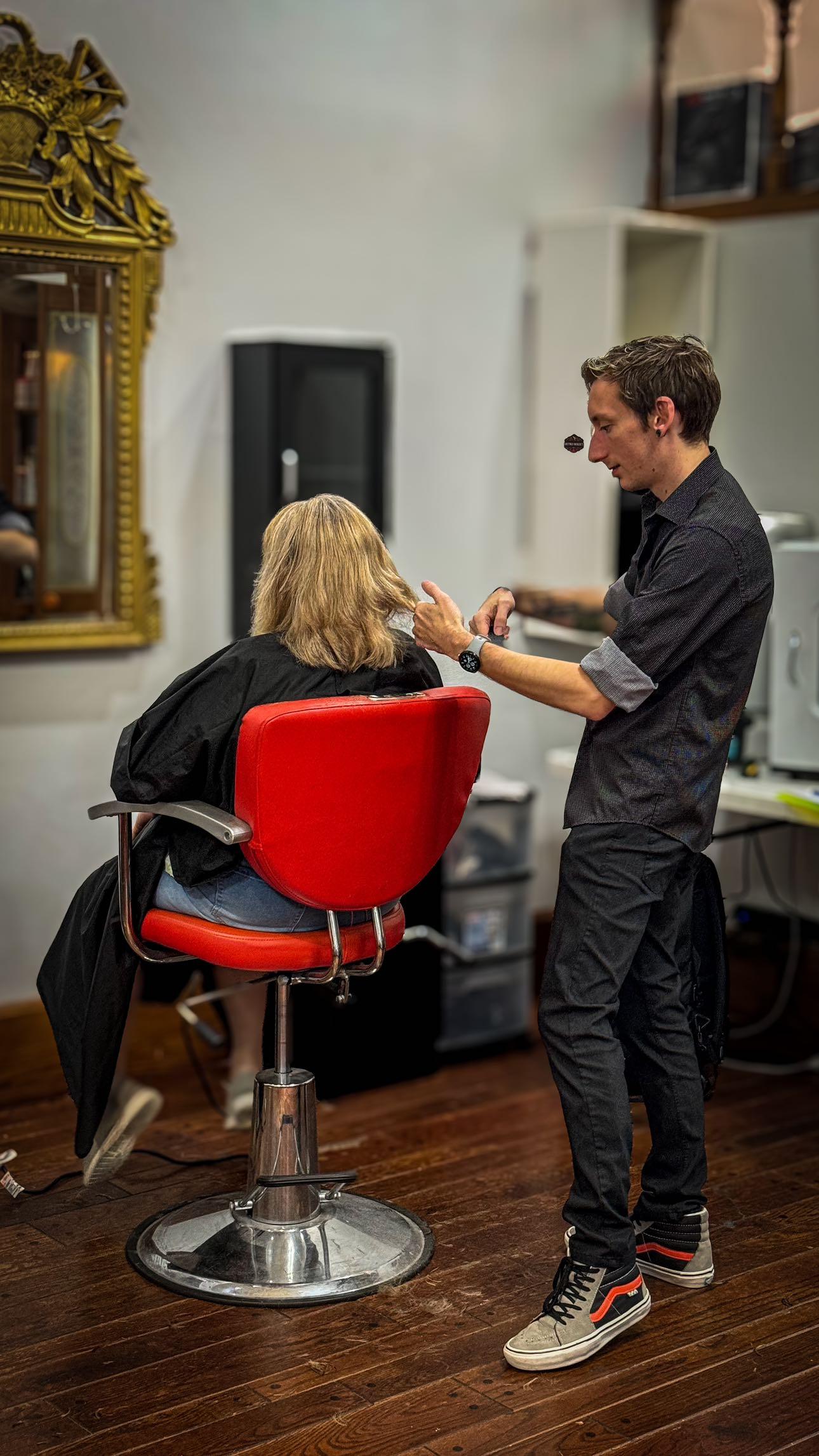 A stylist working on a client's hair in a salon, featuring a red salon chair and a mirror in a vibrant salon environment.